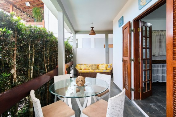 Varanda do chalé com mesa de vidro e vista para o jardim