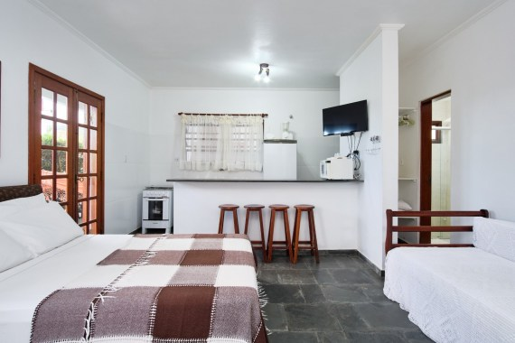 Interior do chalé com cama de casal, cozinha americana e TV